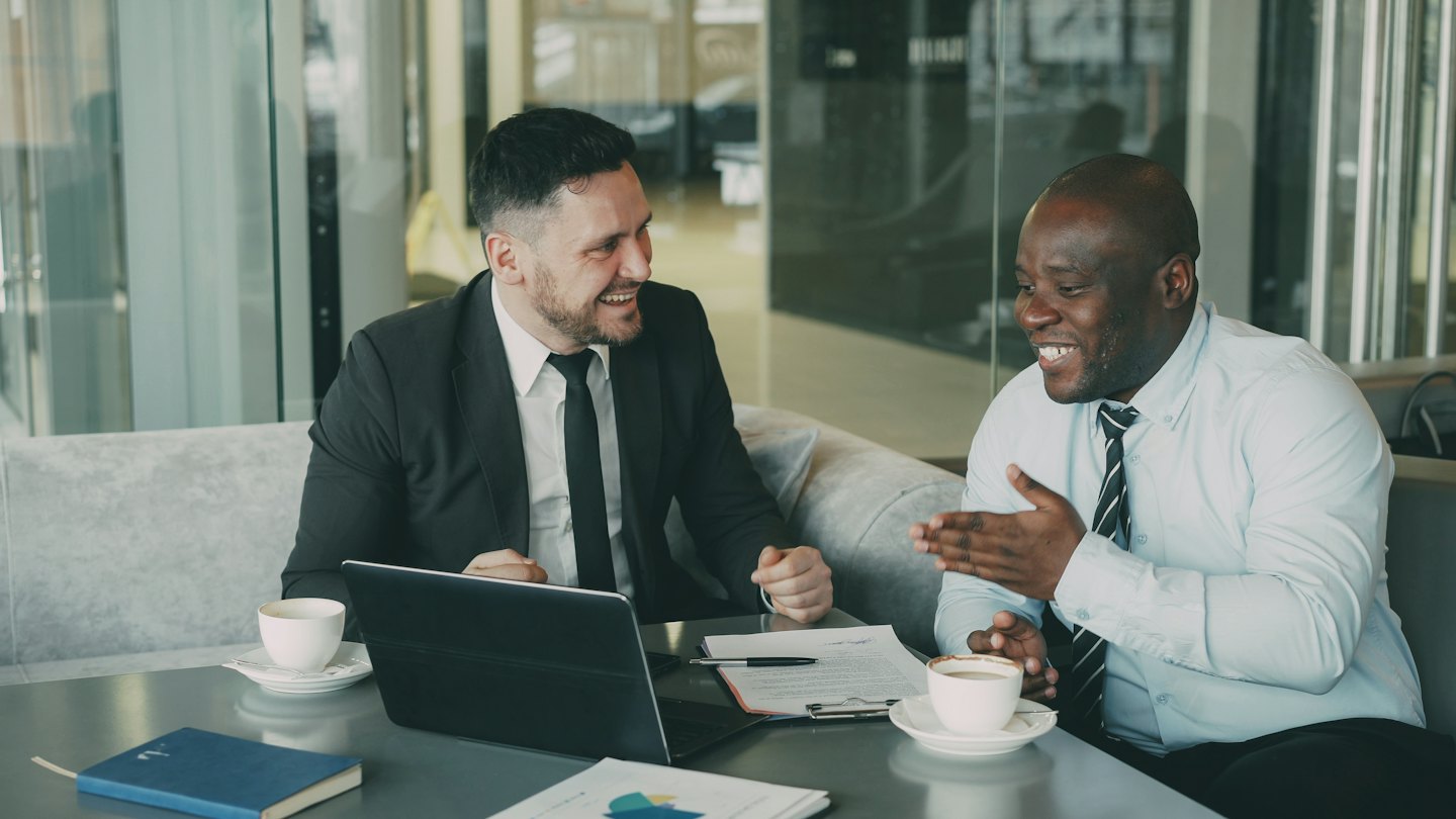 Two businessmen collaborate over coffee and documents at an office cafe.